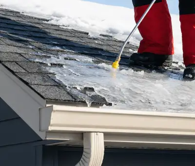 Ice dam removal technician using a steam wand to melt thick ice buildup on a residential roof in Rochester, NY