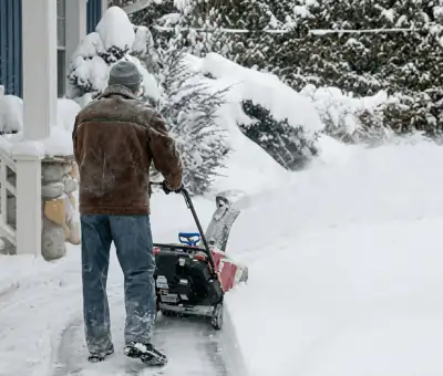 Residential snow removal technician using a snow blower to clear a home driveway and walkway in Rochester, NY